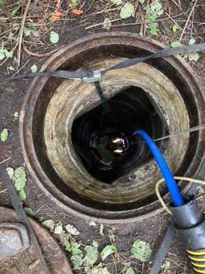 Looking into a deep catch basin.  Contractor setting up CCTV camera on remote control crawler to inspect the storm sewer.
