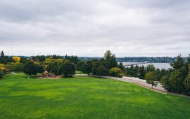 An image of an expansive green park field and playground with a view overlooking Lake Washington