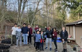 A group of people posing in front of a house with trees in the back.