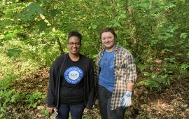 Two volunteers posing in front of a shrub on a sunny day. 