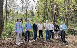 A small group of volunteers posing in front of a sunny forest.