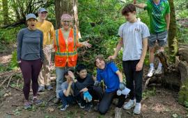 A group of volunteers posing in a forest where they recently cleared ivy. 