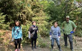 Four volunteers posing in a forest in front of a cleared patch of blackberry. 