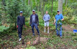 Four volunteers posing in the woods holding ivy they recently removed. 