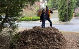 Two volunteers standing on top of a large mulch pile.
