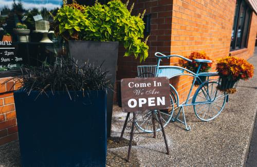 A blue bicycle with flowers in the basket is parked next to a sign that reads "Yes We're Open" outside a flower shop.