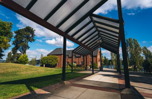 A covered walkway in a park leads to a brick brick building.