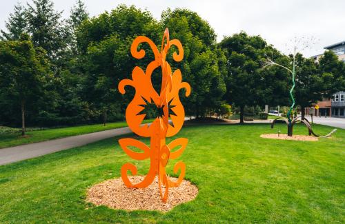 A whimsical and bright orange sculpture blooms in an sculpture park