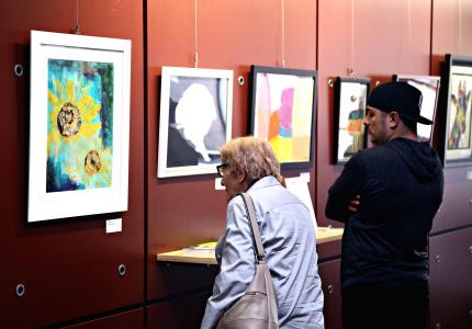 A woman and man view works of two-dimensional art in an indoor art gallery