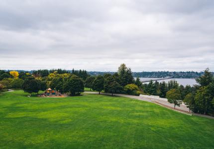 An image of an expansive green park field and playground with a view overlooking Lake Washington