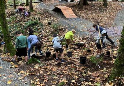 A group of young kids planting small plants in between two gravel paths.
