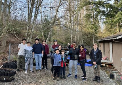 A group of people smiling, standing in front of a forested background. 
