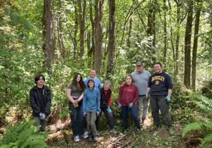 A group of smiling volunteers posing in front of a forest
