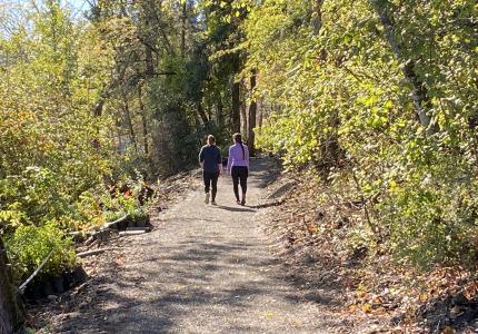Two women walk on a forested, shoreline trail on a sunny fall day in Luther Burbank Park