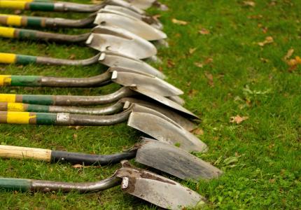 A series of shovels laid out on the grass.