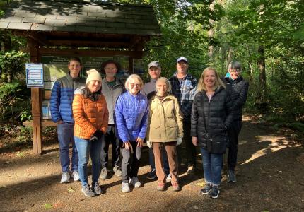 A group of volunteers posing in front of a sign board in a forested park. 