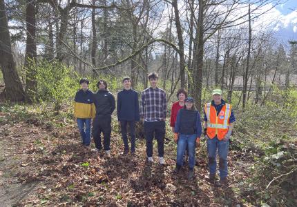 A group of volunteers posing on a sunny day in front of a forest. 