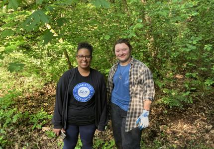 Two volunteers posing in front of a shrub on a sunny day. 