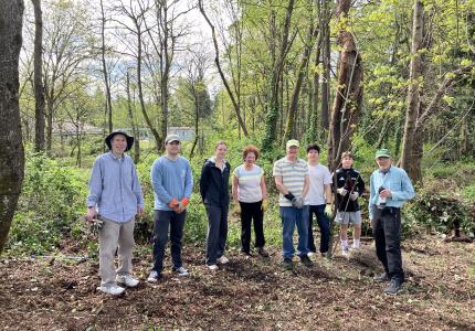 A small group of volunteers posing in front of a sunny forest.