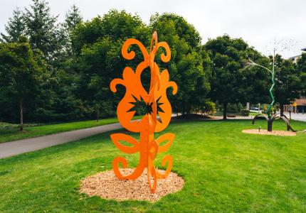 A whimsical and bright orange sculpture blooms in an sculpture park