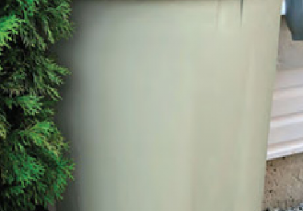 Photo of a tan rain barrel installed under a gutter.