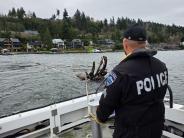 Marine Patrol Sergeant works to remove hazardous log in Lake Washington. Person on a boat next to floating log.