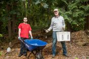 Two volunteers posing, one with a wheel barrow and the other with a bucket to spread mulch.