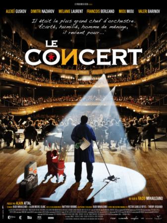 A custodian with a mop and mop bucket stands on a stage looking out a full audience in a big concert hall