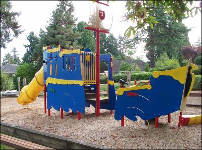 A neighborhood playground that includes a yellow, blue, and red climbing structure themed like a pirate ship.