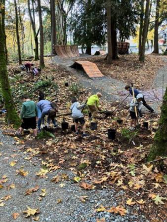 A group of young kids planting small plants in between two gravel paths.