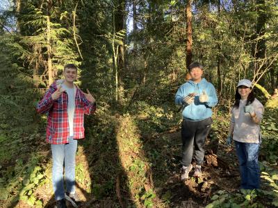 Volunteers posing in front of a pile of pulled up weeds.