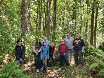 A group of smiling volunteers posing in front of a forest