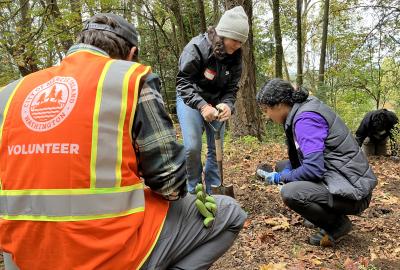 Person in orange vest kneeling down, with two other volunteers.