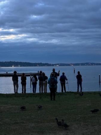 A silhouette of people standing in front of a lake at sunset. 