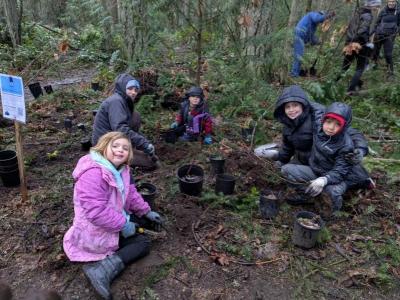 A group of volunteers sitting on the ground next to small native plants
