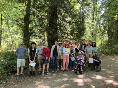 A group of people posing in front of a sunny forest. 