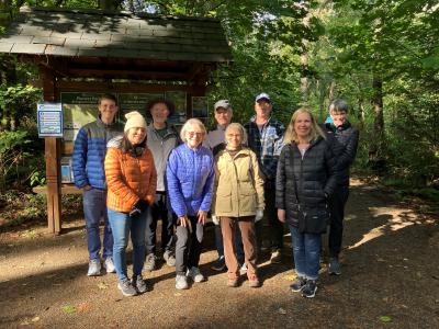 A group of volunteers posing in front of a sign board in a forested park.
