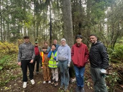 A group of volunteers, posing in a forest with a cloudy sky.