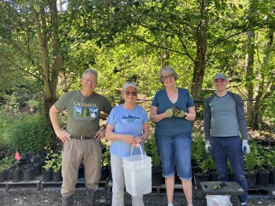A group of volunteers standig in front of trees, smiling and holding tools. 