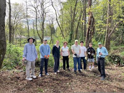 A small group of volunteers posing in front of a sunny forest.