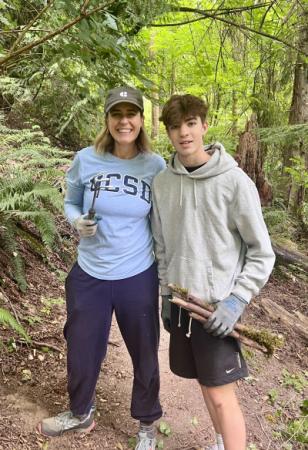 Two volunteers posed holding loppers and pruners standing on a trail in the forest. 