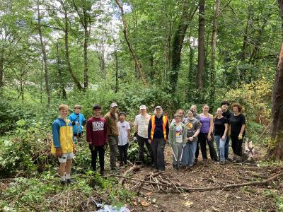 A group of volunteers posing in a forest in front of a pile of pulled up blackberries.