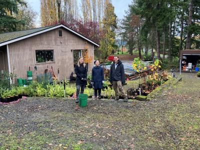 Three volunteers posing and smiling in front of a row of potted plants.