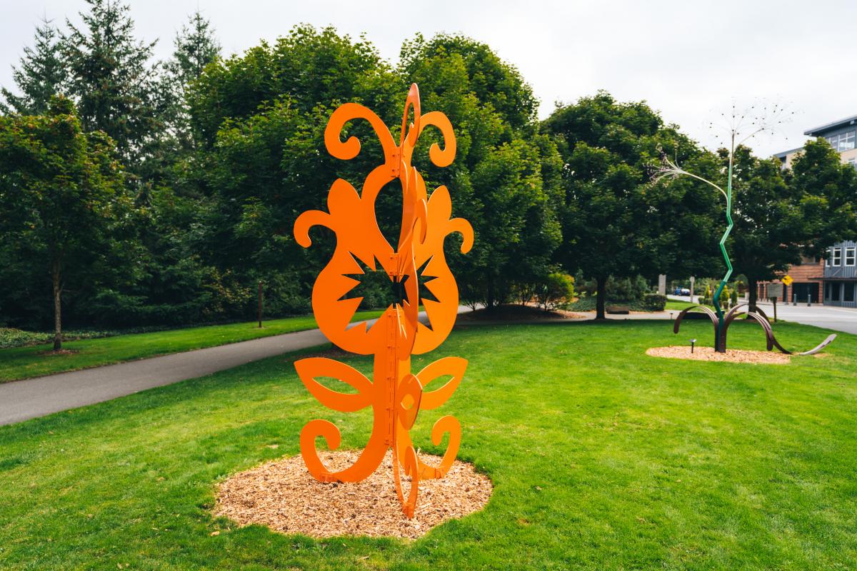 A whimsical and bright orange sculpture blooms in an sculpture park
