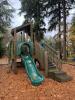 A treehouse playground structure with a green slide sits in a neighborhood park.