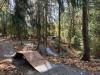 A mountain biking facility with gravel trails and wooden jumps built in a forested area.